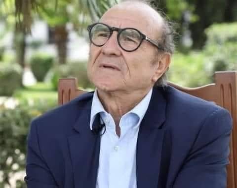 Homme âgé portant des lunettes, en tenue formelle, en plein air.
