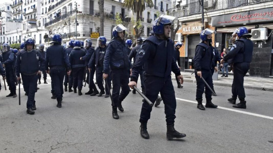 Policiers en uniforme marchant dans une rue urbaine en Algérie.