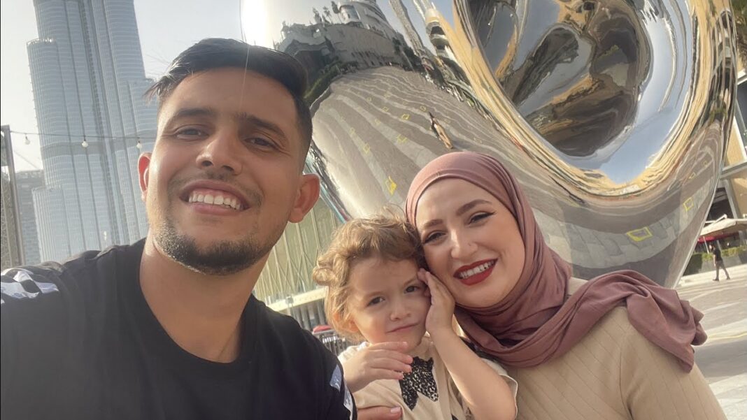 Famille souriante avec un enfant devant une sculpture métallique moderne.
