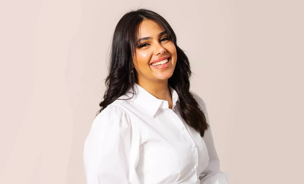 Femme souriante avec cheveux noirs et chemise blanche.