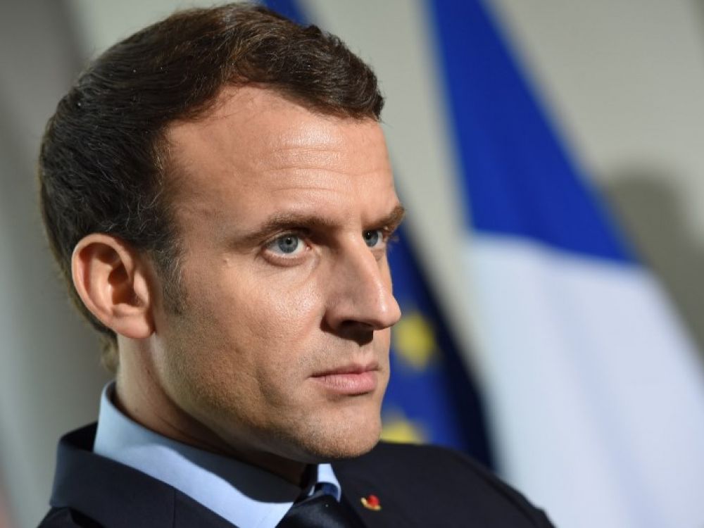 Emmanuel Macron en discussion, drapeau français en arrière-plan.