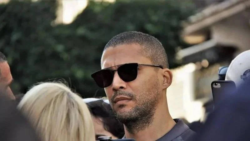 Homme avec barbe et lunettes de soleil dans une foule.