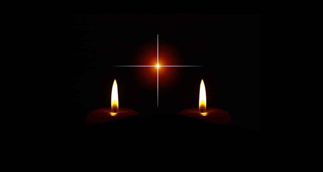 Cierges allumés avec croix lumineuse dans l'obscurité.