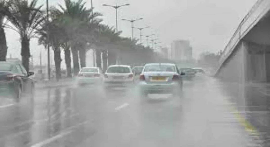 Voitures sous une pluie intense sur une route urbaine en Algérie.