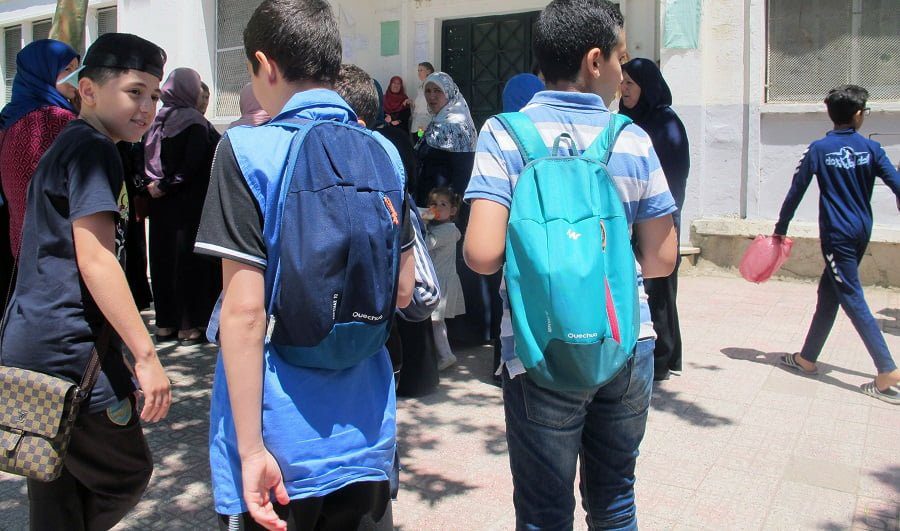 Groupe d'élèves avec sacs à dos devant une école à Tizi Ouzou.