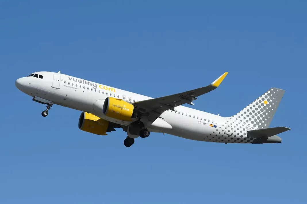 Avion Vueling blanc et jaune en vol dans le ciel bleu.