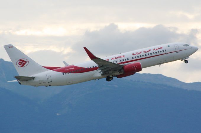 Avion d'Air Algérie en vol dans le ciel avec montagnes en arrière-plan.