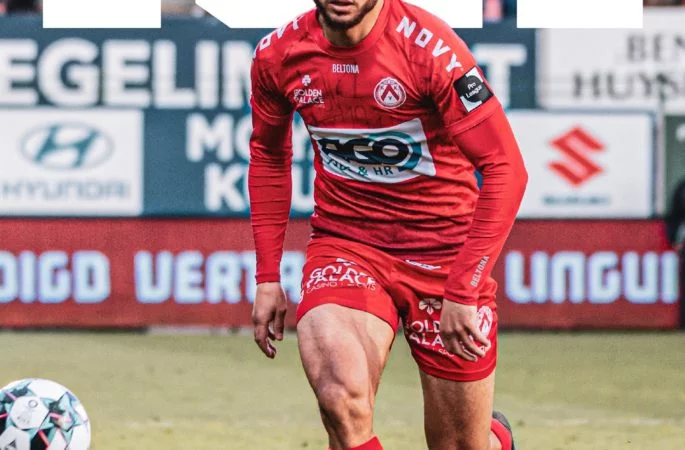 Joueur de football en action portant un maillot rouge sur le terrain.