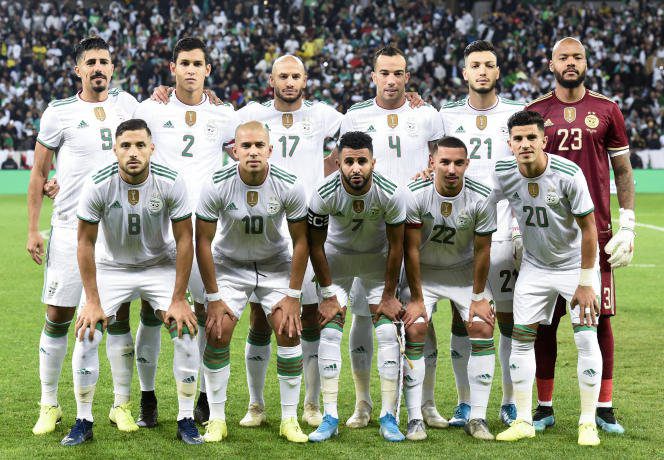 Groupe de joueurs de football algériens en tenue blanche sur le terrain.
