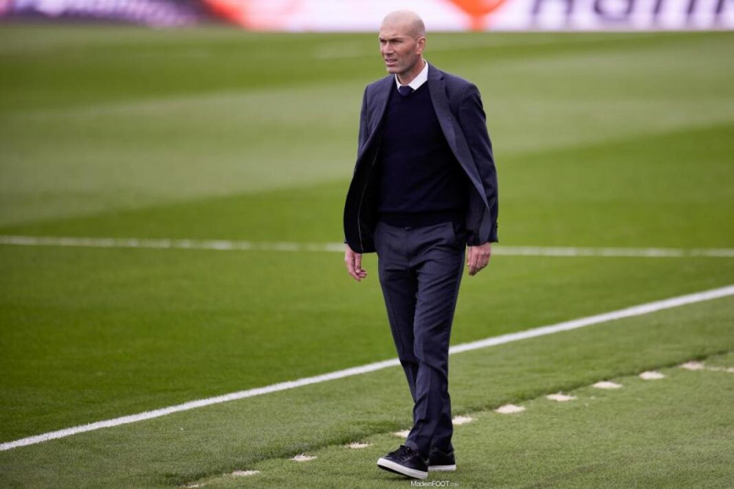 Zidane marchant sur le terrain de football en costume.
