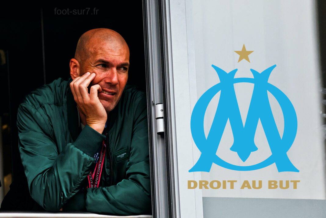 Zinedine Zidane à l’OM ? Zinedine Zidane regardant pensivement par une fenêtre avec logo OM.