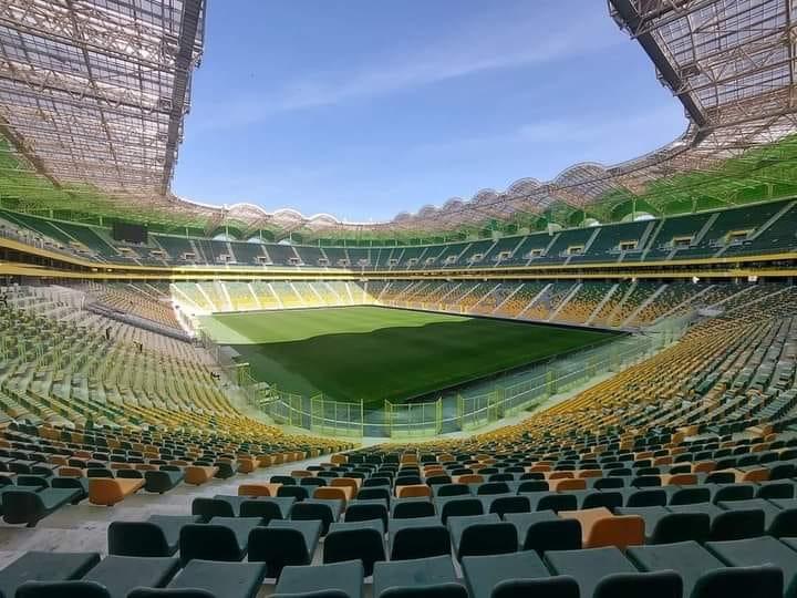 Stade moderne avec sièges colorés et terrain vert au centre.