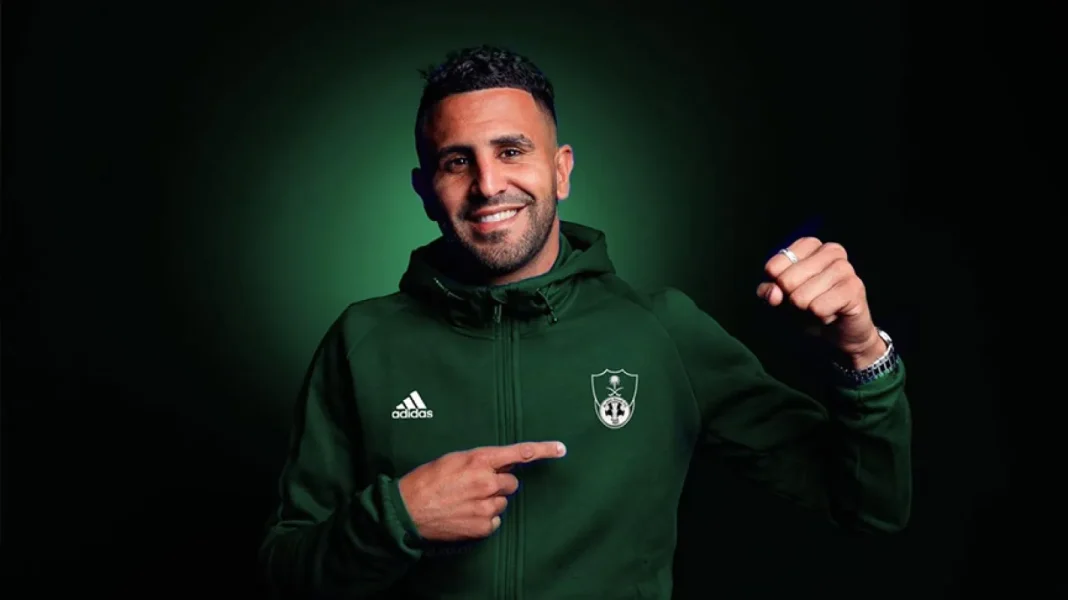 Mahrez souriant en tenue de football verte avec logo de son équipe.
