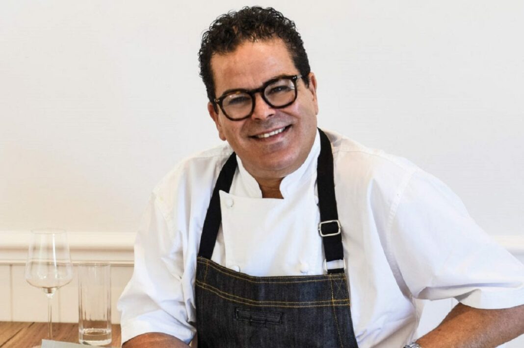 Chef Pierre Khodja souriant en tenue de cuisine avec un verre à côté.
