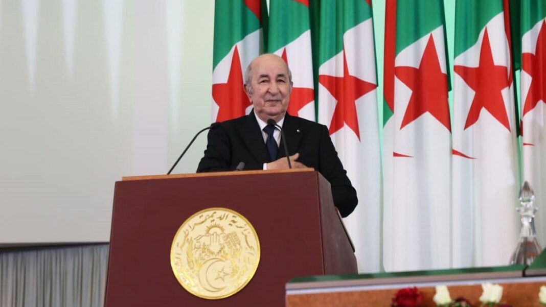 Président Tebboune parlant à un podium avec drapeaux algériens en arrière-plan.