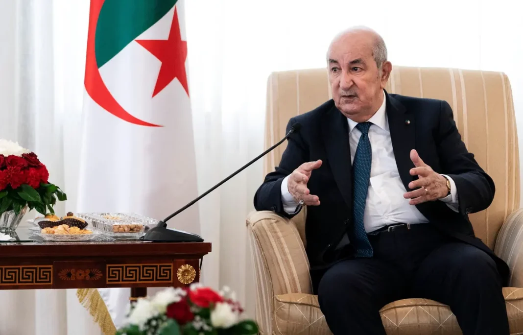 Chef d'État algérien lors d'une réunion diplomatique avec drapeau algérien en arrière-plan.