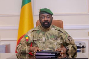 Officier militaire en uniforme avec drapeau du Mali en arrière-plan.