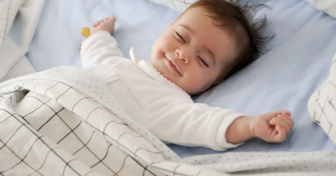 Bébé souriant endormi dans son lit avec une couverture blanche.