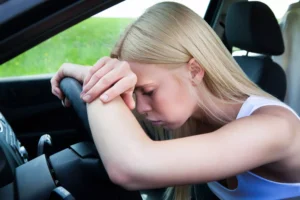 Femme stressée dans une voiture, visage inquiet, mains sur le volant.