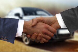 Poignée de main entre deux personnes d'affaires devant une voiture.