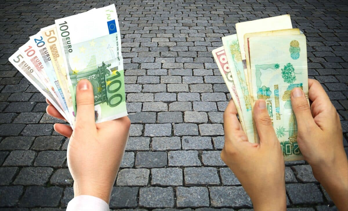 Deux mains tenant des billets de banque en euros et dinars algériens.