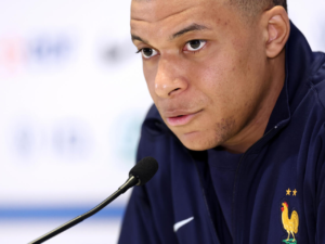 Kylian Mbappe à une conférence, concentré et sérieux.