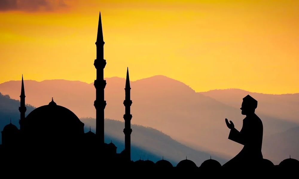 Silhouette d'une mosquée et d'une personne en prière au coucher du soleil.
