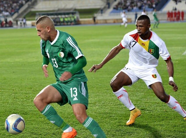 Joueur de Guinée et joueur d'Algérie en action lors d'un match de football.