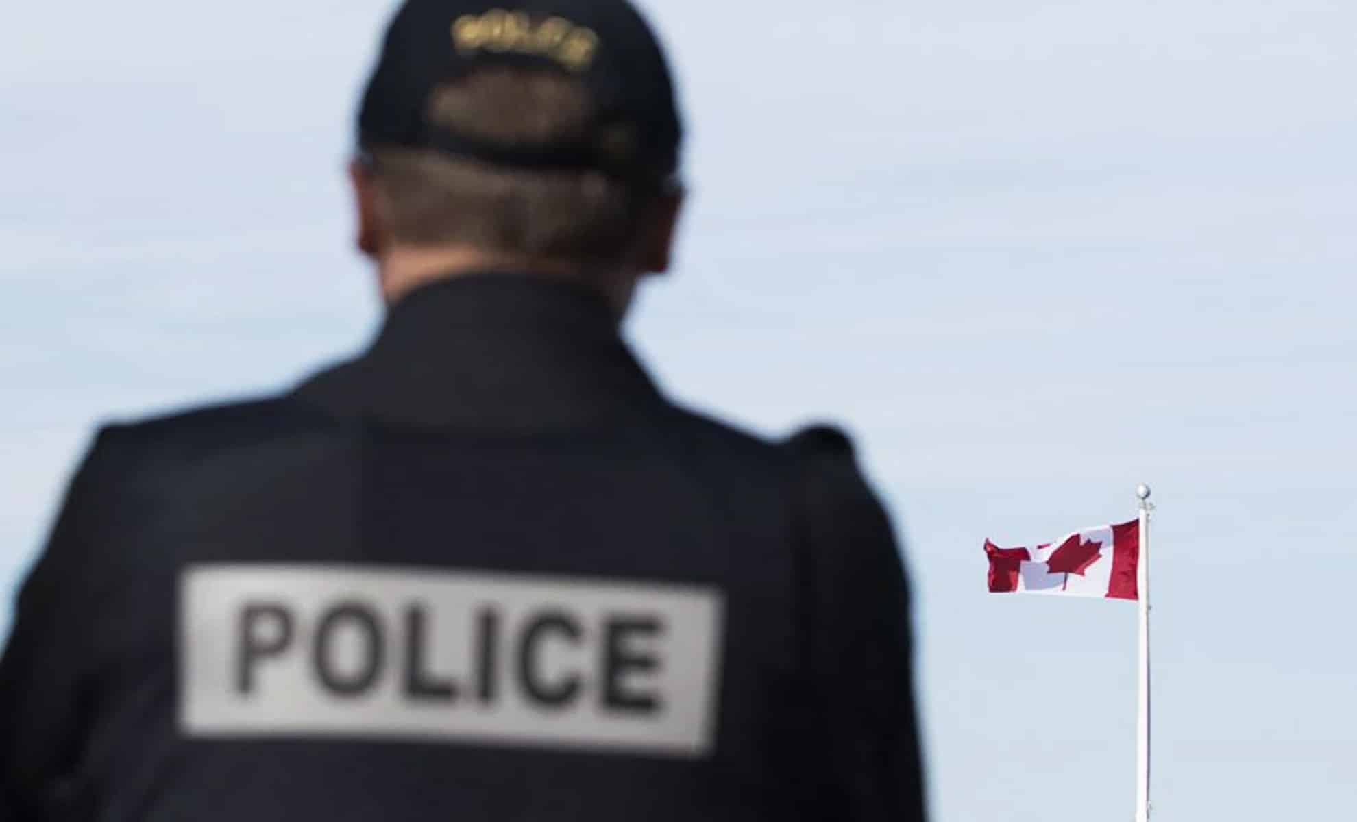 Agent de police observant un drapeau canadien en arrière-plan.