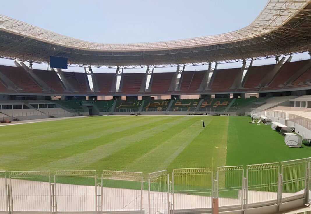 Stade de Douera vide avec pelouse bien entretenue et tribunes modernes.