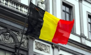 Drapeau belge en tissu flottant devant un bâtiment historique.