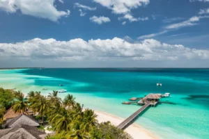 Vue aérienne d'une plage tropicale avec eaux turquoise et pont en bois.