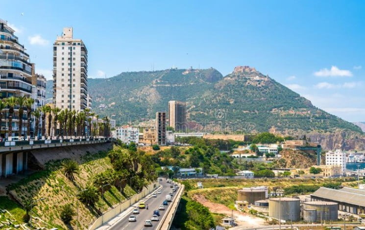 Vue panoramique d'Oran avec bâtiments, montagnes et ciel bleu.