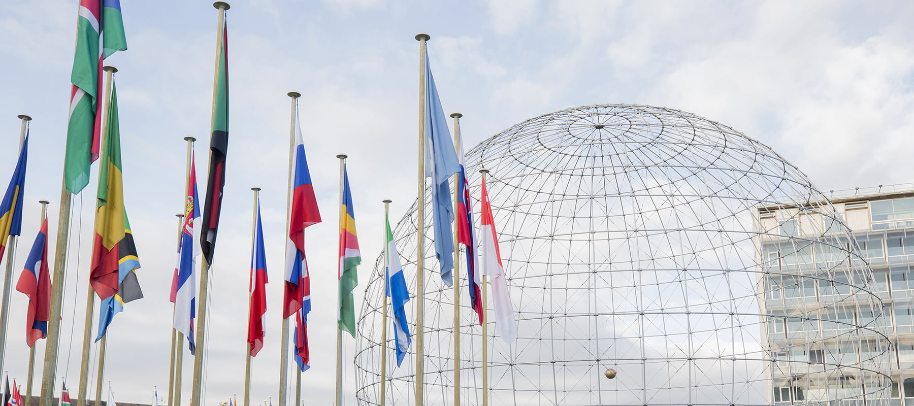 Drapeaux de différents pays devant une structure géodésique en verre.