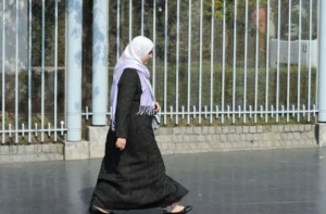 Femme en hijab marchant près d'une clôture en métal en France.