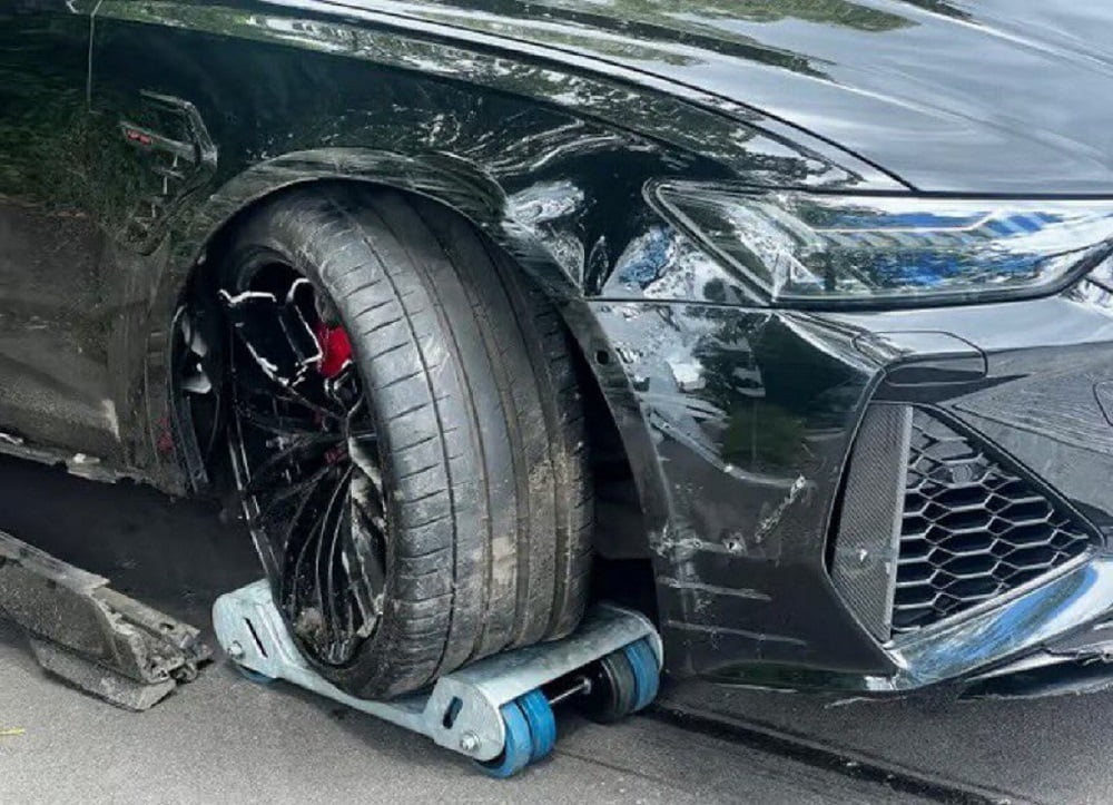 Voiture noire avec roue endommagée et débris sur la route.