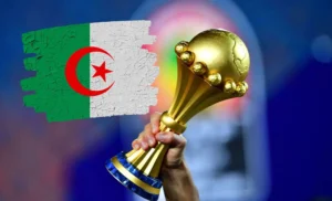 L’organisation de la CAN confiée à l’Algérie par la CAF? Les révélations explosives de Mazouzi ravivent les flammes d'un dossier brûlant Main tenant la coupe de la CAN avec drapeau algérien en fond.