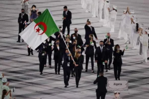 Groupe d'athlètes algériens en tenue de cérémonie avec drapeau national.