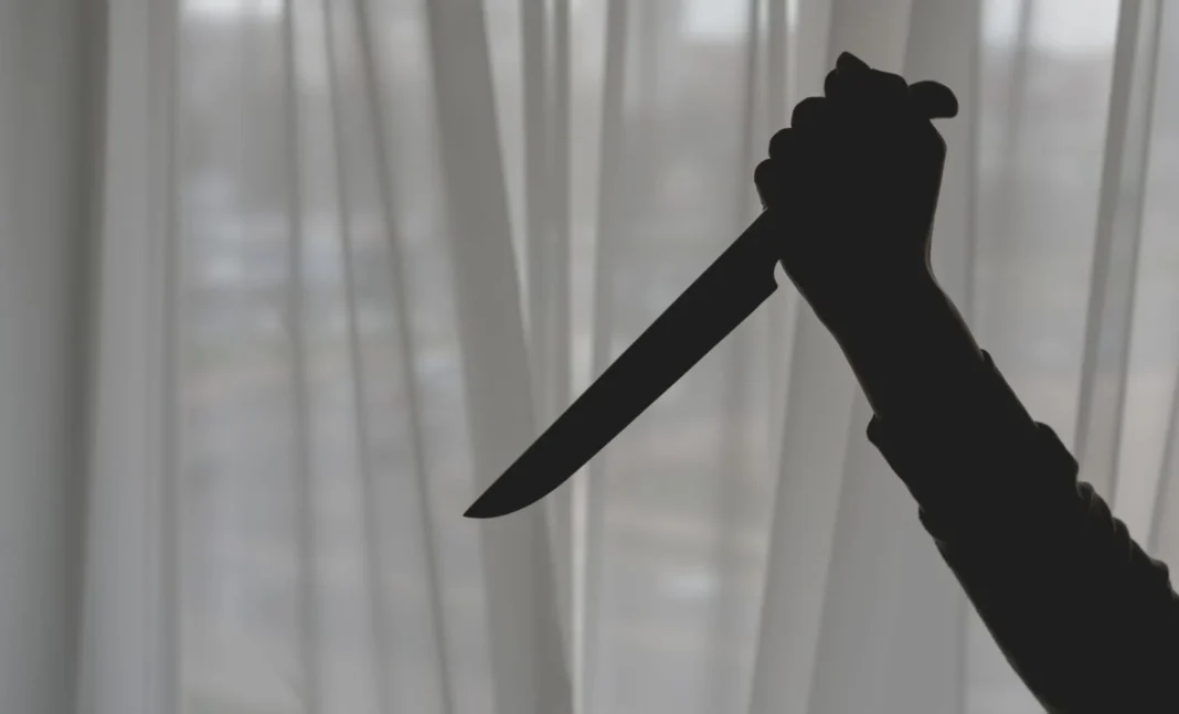 Silhouette d'un couteau tenu par une main contre une fenêtre.