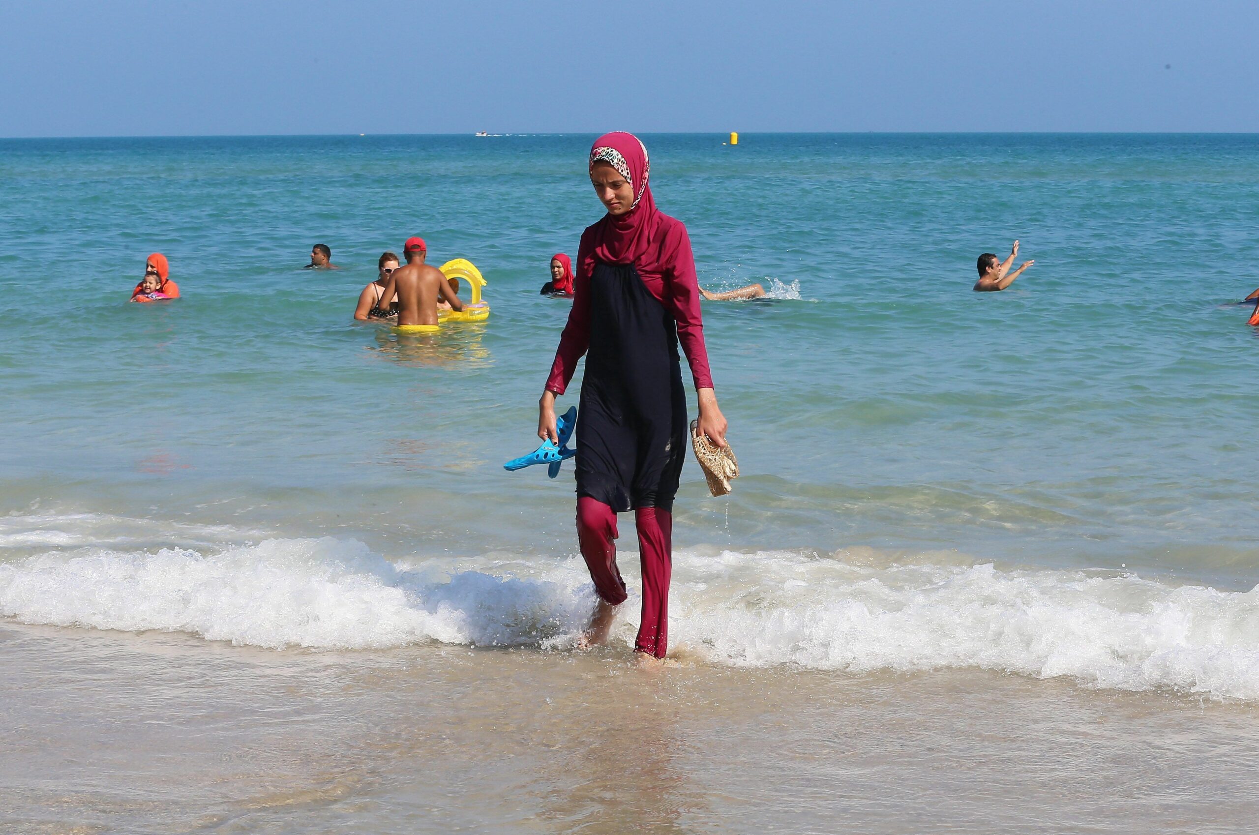 Femme en burkini marchant sur la plage ensoleillée.