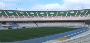 Stade 5 Juillet avec pelouse endommagée et tribunes vides.