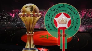 Qualif/CAN 2025 au Maroc : Très bonne nouvelle pour l'Algérie شعار الاتحاد الملكي المغربي لكرة القدم مع كأس أفريقيا في ملعب مغطى بالأضواء.
