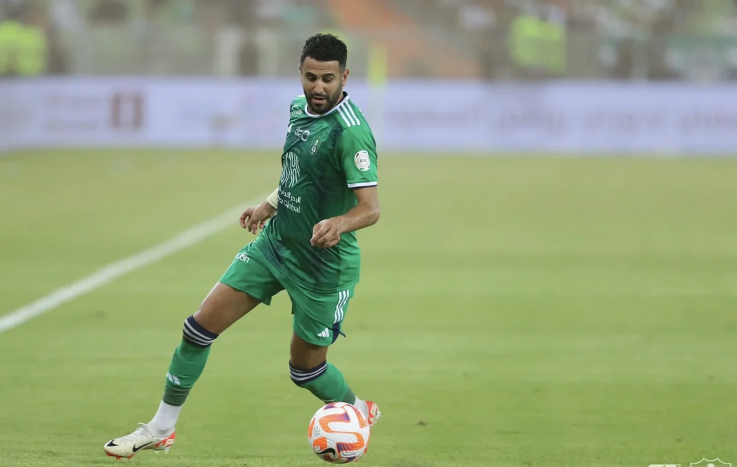 Riyad Mahrez en tenue verte sur le terrain avec un ballon de football.