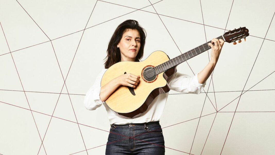 Femme avec guitare acoustique, expression concentrée.