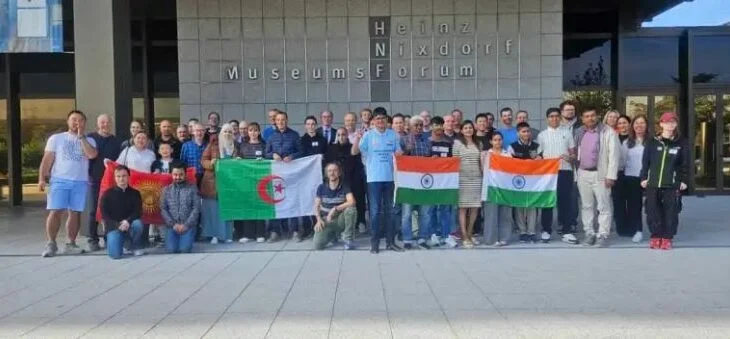 Groupe de personnes avec drapeaux algérien, indien et ouzbek devant un musée.