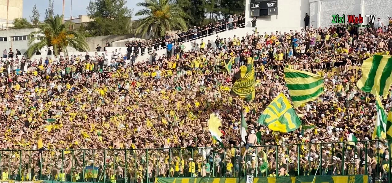Supporters du JSK avec drapeaux verts et jaunes en tribune.