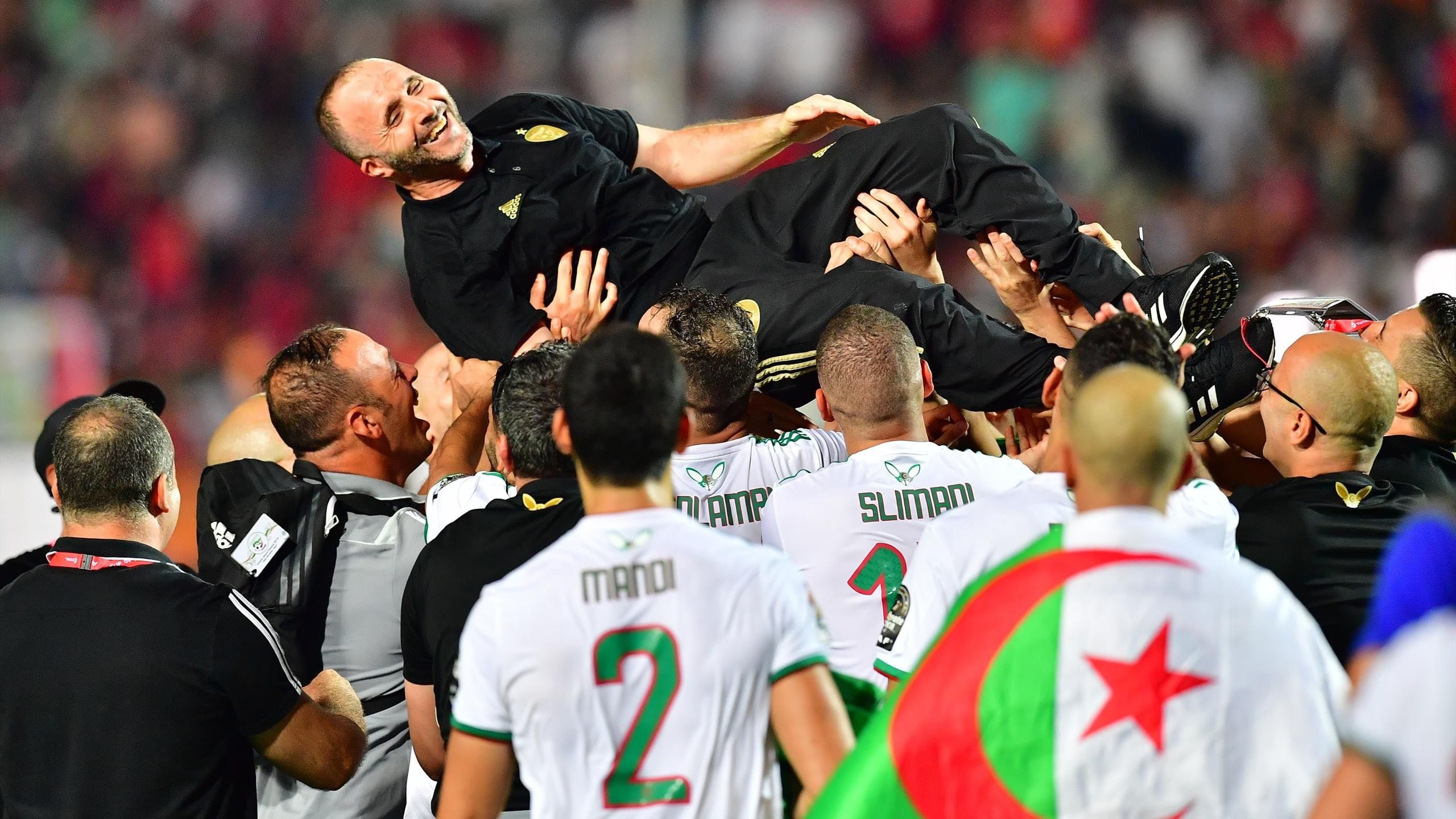 Djamel Belmadi porté par ses joueurs lors d'une célébration sportive.