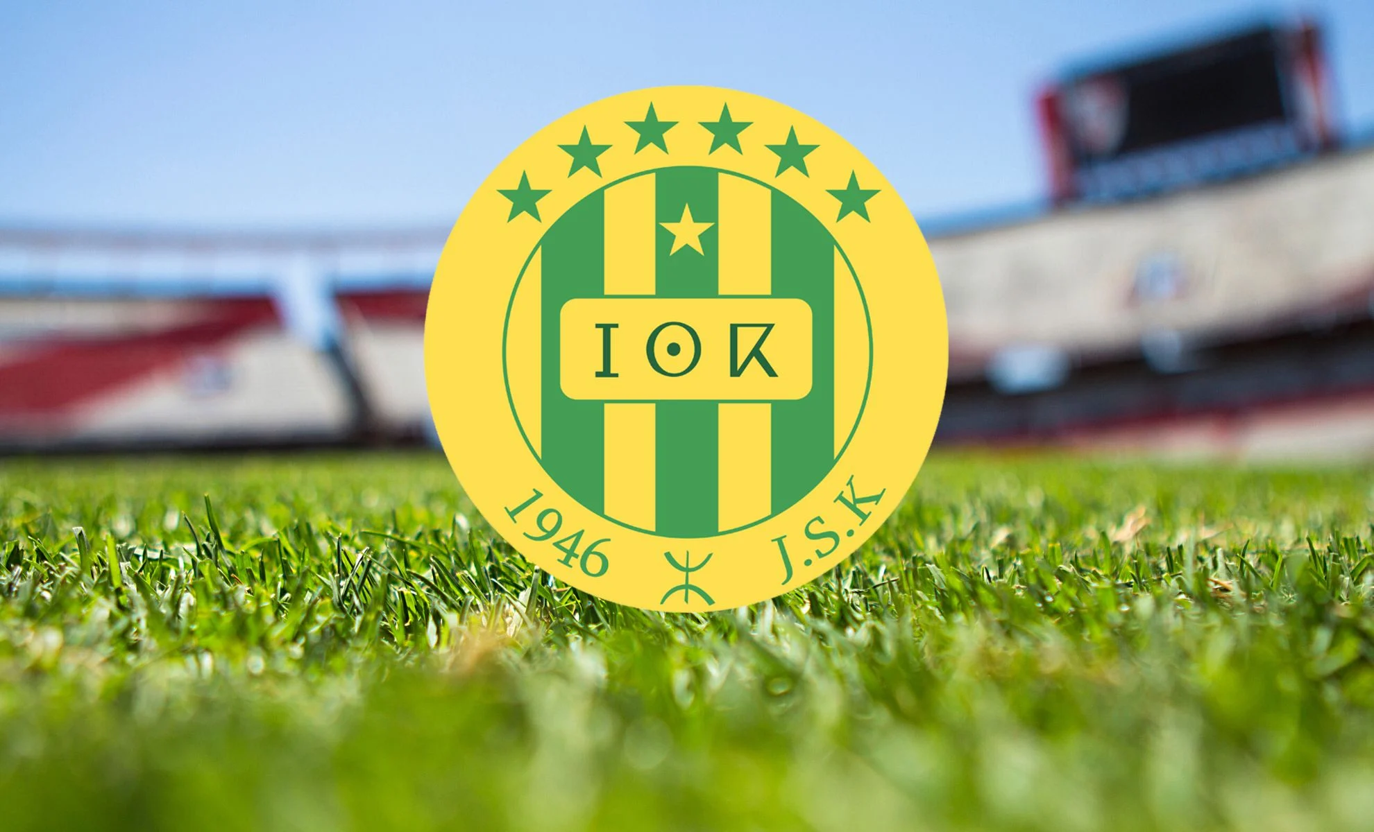 JS Kabylie en Ligue 1 2024-2025 : un parcours contrasté à domicile et à l'extérieur Logo du JS Kabylie sur le terrain de football en plein air.