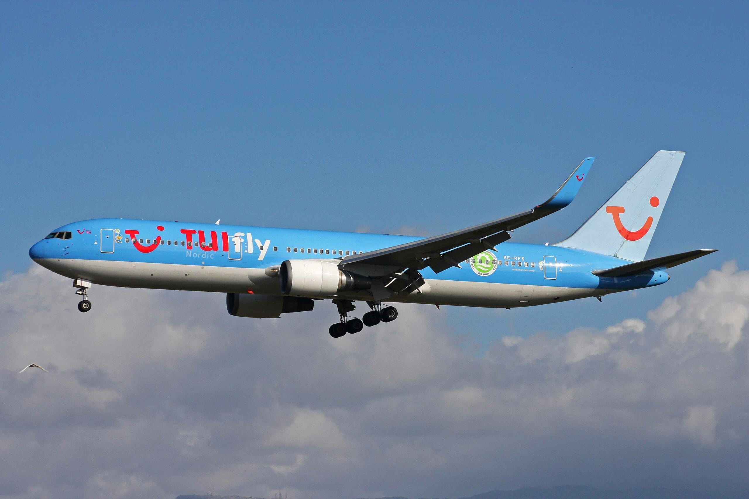 Avion TUI Fly bleu en vol dans le ciel avec nuages.