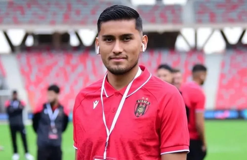Jeune joueur de football avec écouteurs, en tenue USM Alger, dans un stade.